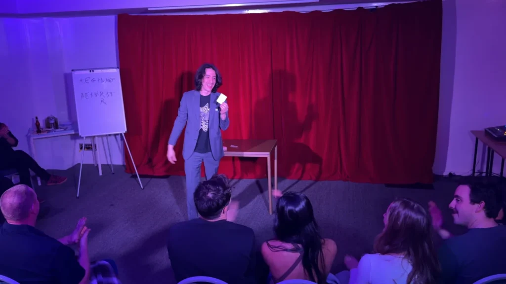 Sebastián performing card magic as seated audience members applaud.